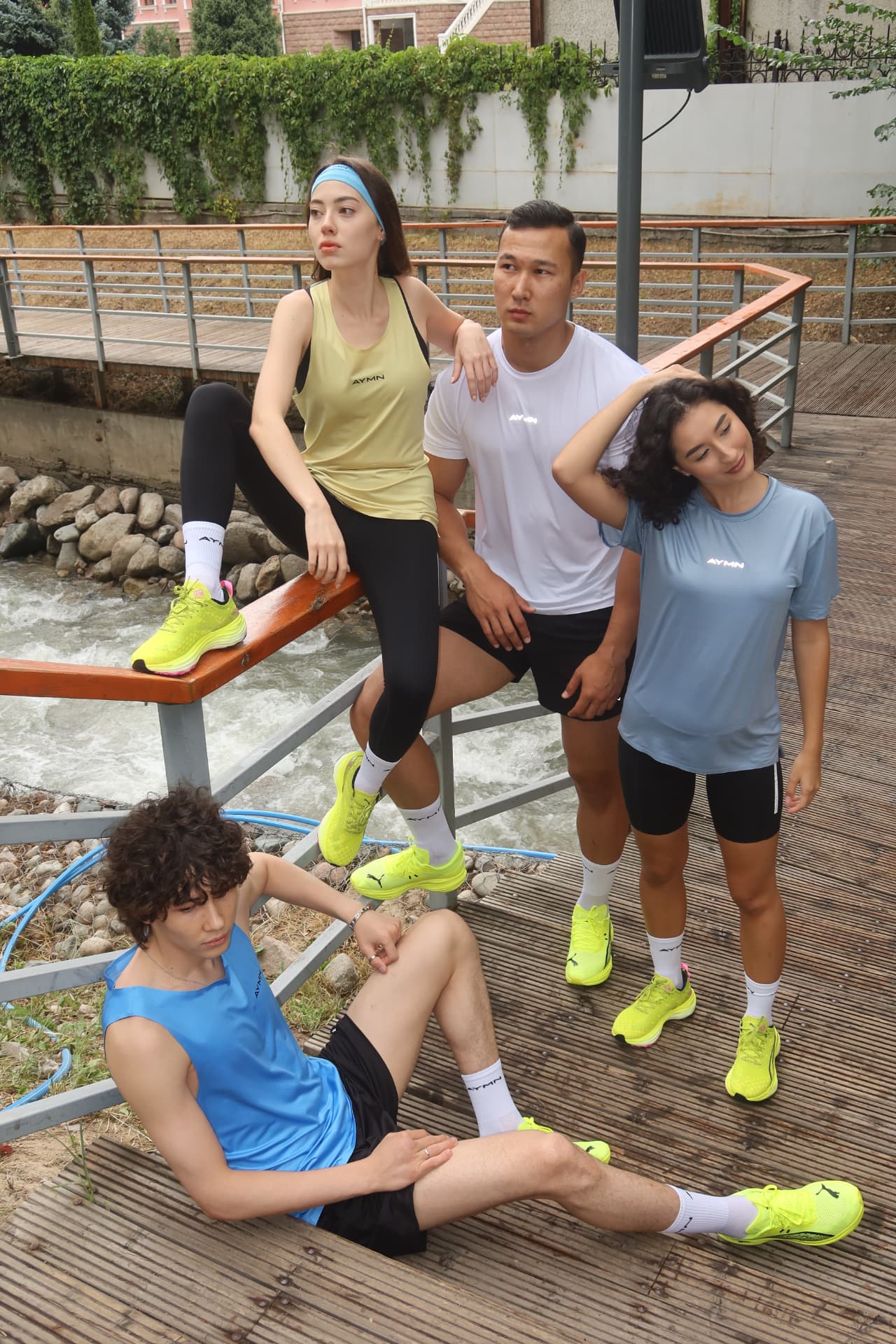 Four models in running gear posing on a wooden deck by a stream